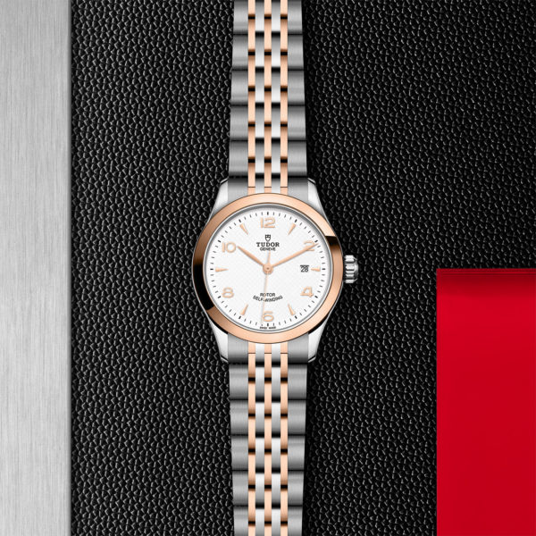 TUDOR 1926 Watch with a 28mm Steel Case, Rose Gold Bezel (M91351-0009) Flat lay on black and red background