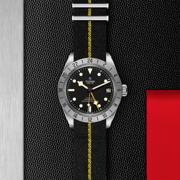TUDOR Black Bay Pro Watch with 39mm Steel Case, Black Fabric Strap With Yellow Band (M79470-0002) Flat lay on black and red background