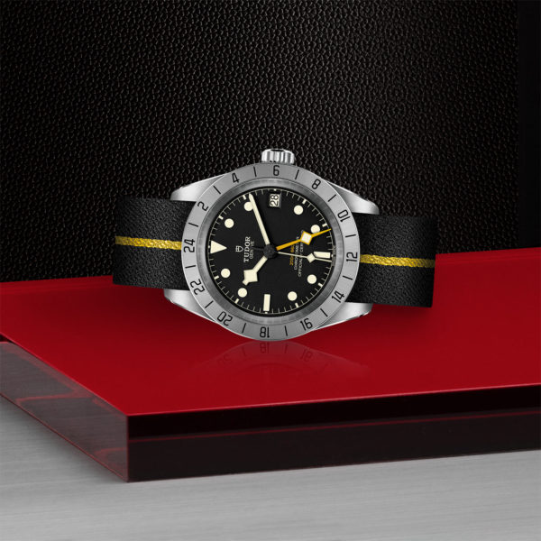 TUDOR Black Bay Pro Watch with 39mm Steel Case, Black Fabric Strap With Yellow Band (M79470-0002) Laying Down on Red Tray