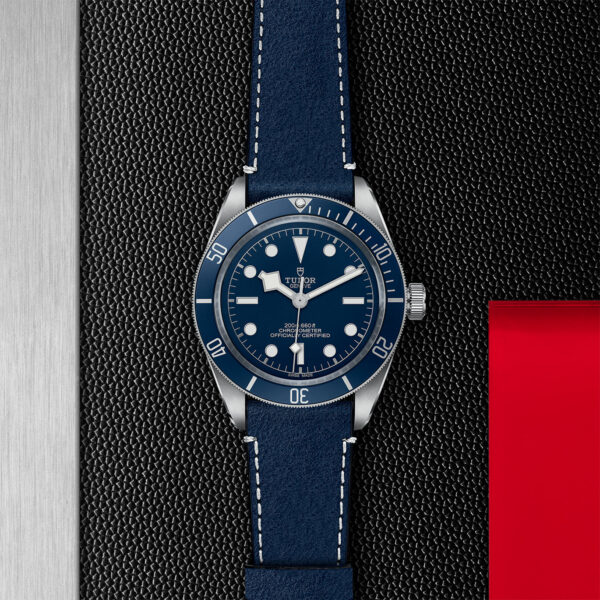 TUDOR Black Bay Fifty-Eight Watch, with a 39mm Steel Case, Blue 'Soft Touch' Strap (M79030B-0002) Flat lay on black and red background