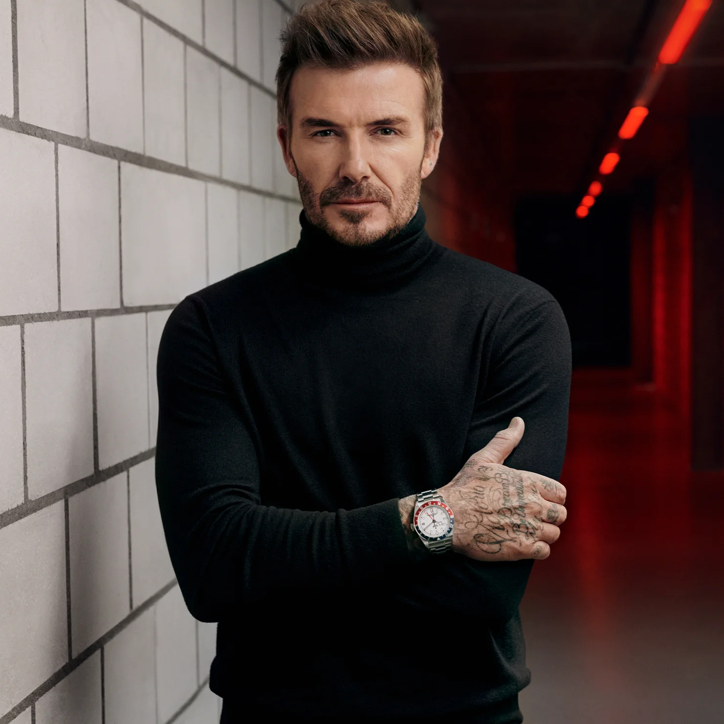 TUDOR Ambassador David Beckham in hall next to brick wall and red lighting