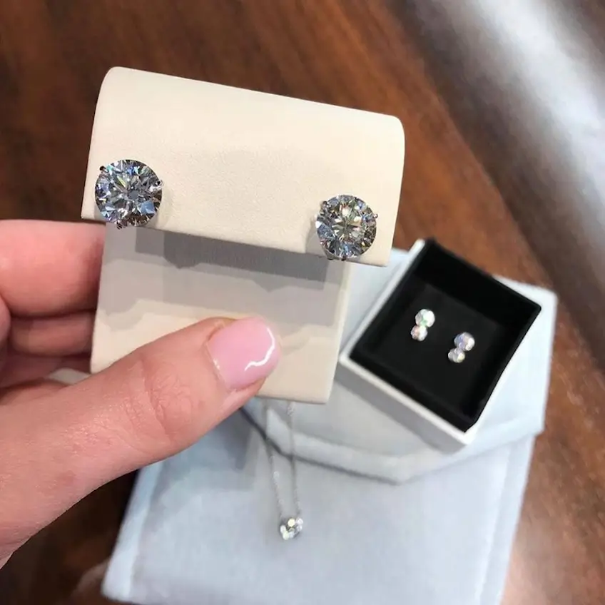 woman holding a pair of diamond stud earrings