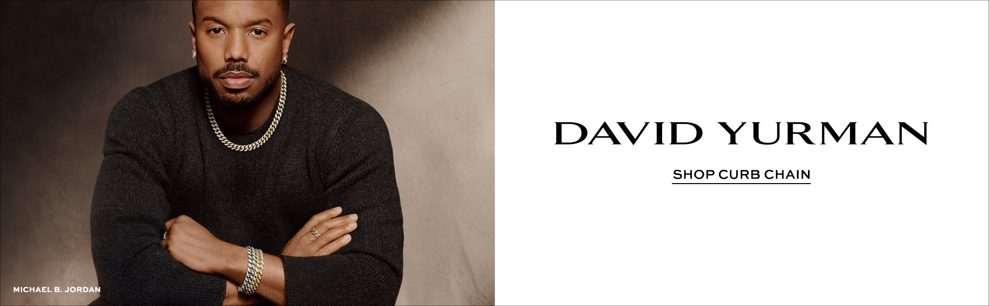 Promotional banner featuring Michael B. Jordan wearing layered David Yurman curb chain necklaces, bracelets, rings, and earrings in mixed metals while posing in a dark knit sweater against a warm neutral background. The right side of the image features the David Yurman logo with the text “Shop Curb Chain” on a clean light background.