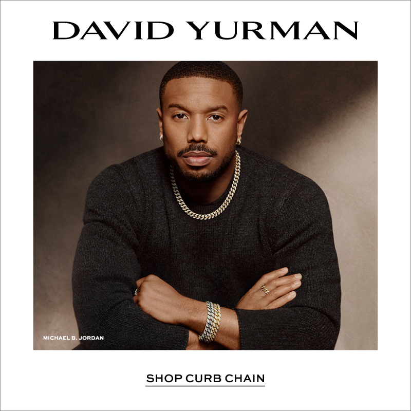 Square David Yurman promotional image featuring Michael B. Jordan wearing layered curb chain necklaces, bracelets, rings, and earrings in mixed metals with a dark knit sweater against a warm neutral backdrop. The David Yurman logo appears at the top with “Shop Curb Chain” text below the portrait.