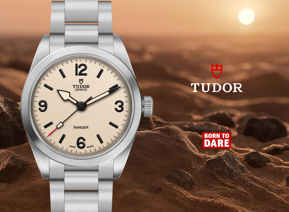 TUDOR Ranger watch featuring a cream dial, bold black Arabic numerals, stainless steel case and bracelet, displayed against a rugged mountain landscape with the TUDOR and Born to Dare logos.